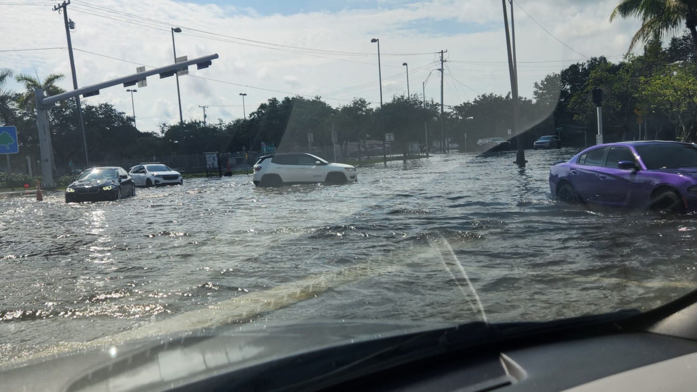 Cars sit in deep floodwater across an intersection, seen through a driver's windshield.