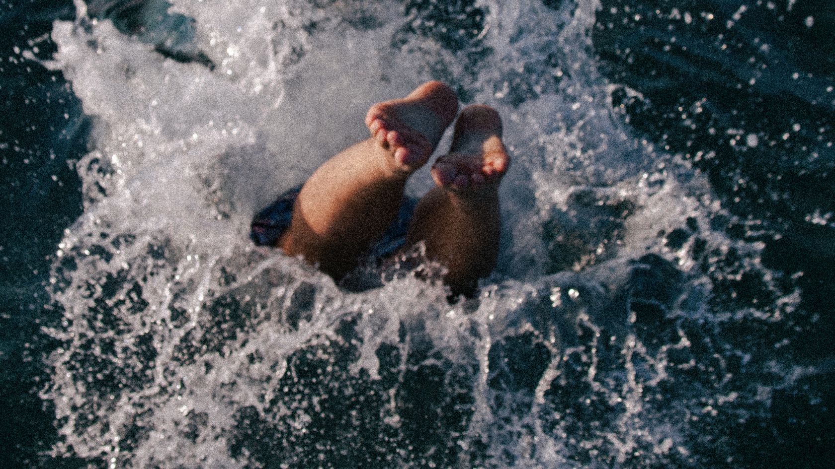 Overhead view of a child's bare feet kicking up whitewater in breaking surf.