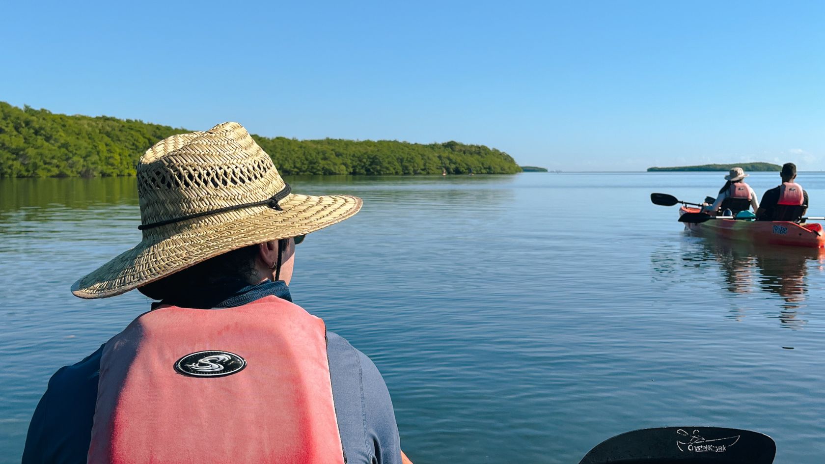 Paddler's view from a kayak of a second kayak and mangrove islands on calm water.
